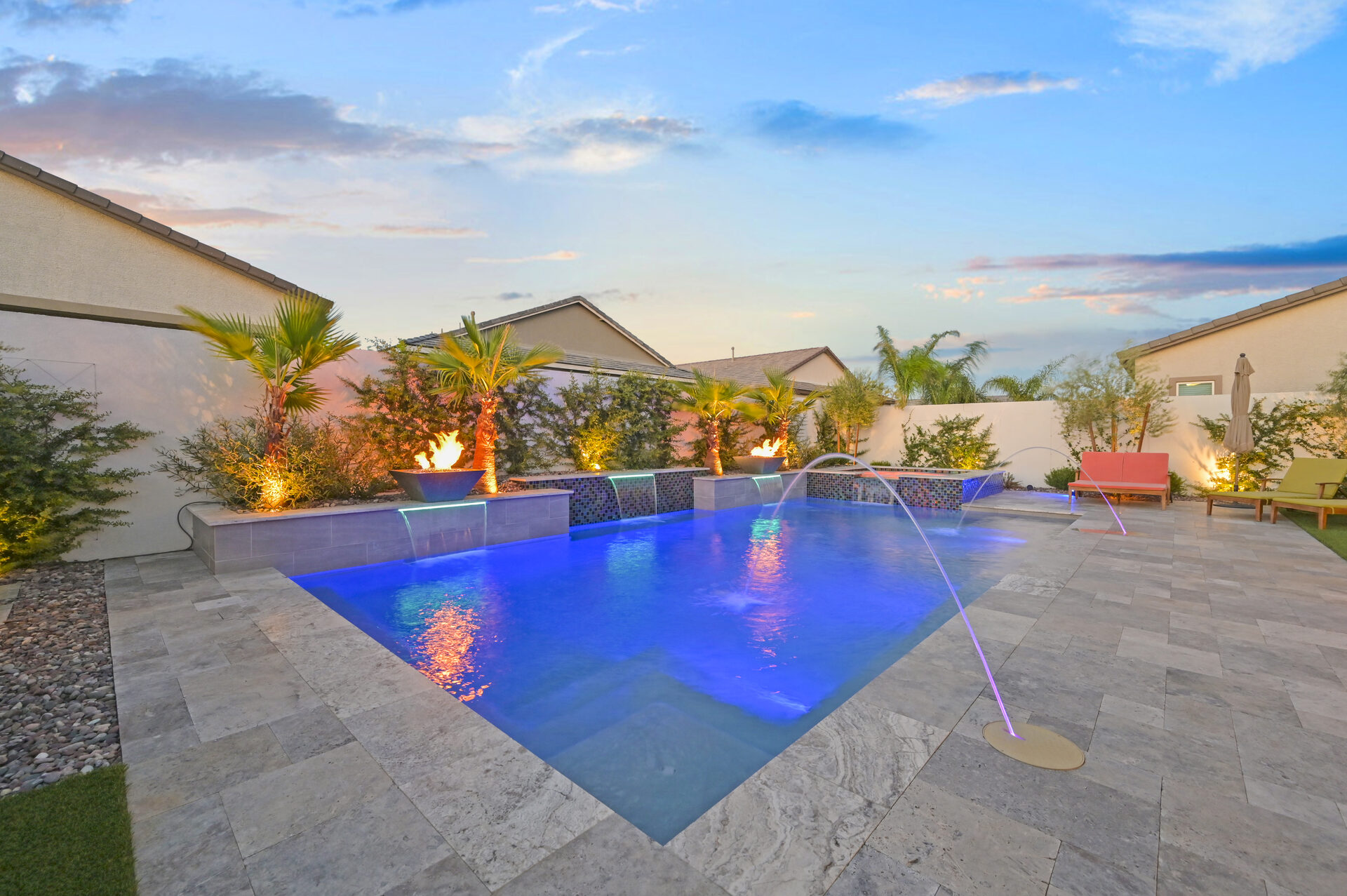 Pool with laminar deck jets, fire bowls, and colorful glass mosaic spa at dusk